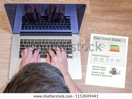 Senior man typing on laptop with a credit report and credit freeze option on desk