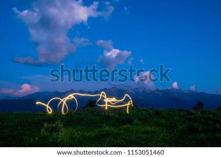 freezelight drawing by light of a LED flashlight in the air with mountains and sky in the background