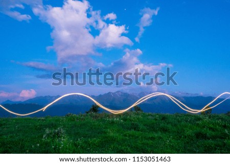 freezelight drawing by light of a LED flashlight in the air with mountains and sky in the background