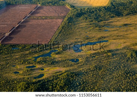 Extraction of peat( brown area field) from bog in Estonia, Northern Europe in dusk in summer. Due to scratches and reflections on plane`s window, there are few blurred spots on picture.