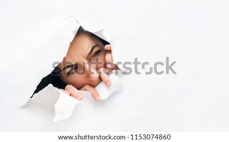 Portrait of a woman looking through the hole in white paper. Distrustful look. Women's curiosity and gossip. A jealous wife. Royalty-Free Stock Photo #1153074860