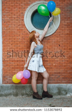 Young woman with colorful balloons on a brick wall background. 