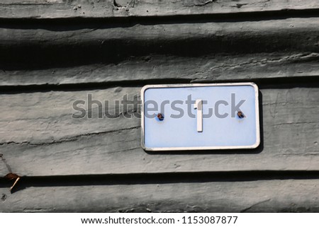 Close up outdoor view of the number one written in white on a blue rectangular metallic plate. Indication of the address in a french urban street. Isolated numerical sign fixed at a wooden facade.
