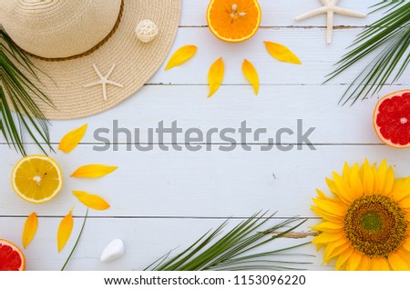 Space for lettering surronded by beatiful objects frame with a summer hat, palm leaves, fresh citrus fruits, sunflowers and sea stars on white wooden background. Flat lay, top view, copy space mock up