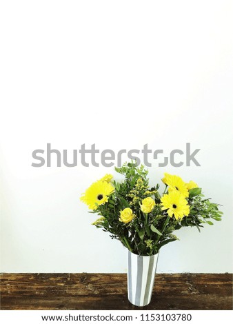 beautiful bunch of fresh yellow flowers in vase on wooden floor against white wall.