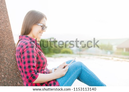 Cheerful young female student with cute smile typing write message on smart phone. Girl with a mobile phone in her hands sitting on the steps in the park.