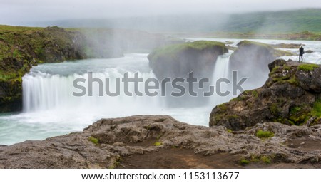 A photographer with a tripod taking a show shutter speed image of the Magestic Godafoss Waterfall in North Iceland