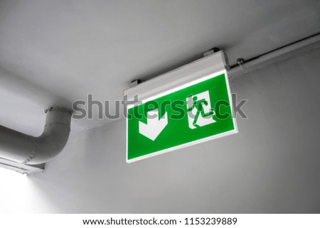 Green emergency exit sign. Direction to the escape way hanging on ceiling.