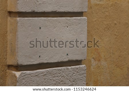 Close up outdoor view of part of an ancient wall painted in ochre, with a vertical column made of rectangular bricks. Abstract architectural image of a rough textured surface with parallel lines. 
 