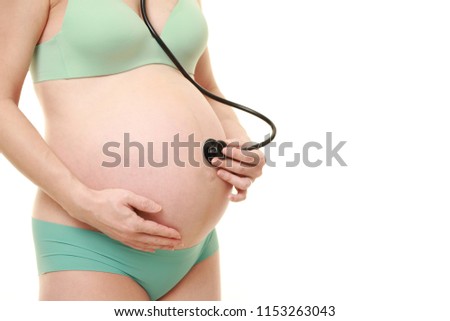 studio shot of pregnant woman wearing green underwear examining belly with stethoscope isolated on white
