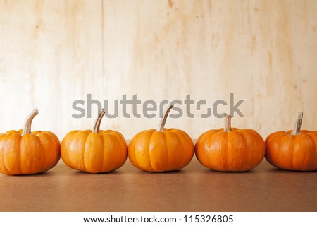 Five orange pumpkins sit in a row in front of a distressed, wooden background.