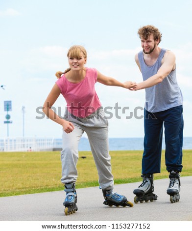Active lifestyle people and freedom concept. Young fit couple on roller skates riding outdoors on sea coast, woman and man enjoying time together.