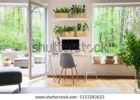 Inspirational workspace interior for a freelancer with computer on a wooden desk, white walls and the view of nature in the backyard outside Royalty-Free Stock Photo #1153283623
