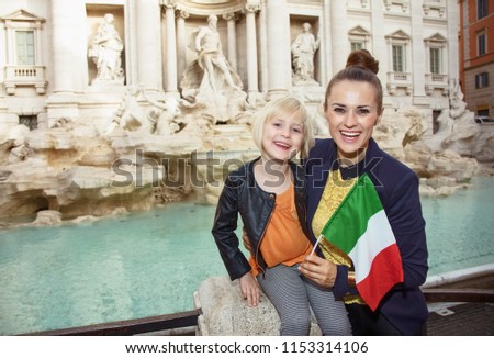 happy young mother and child travellers with Italian flag against Trevi Fountain