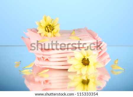 Panty liners in individual packing and yellow flowers on blue background close-up