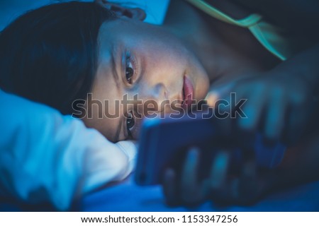 Little girl lying on bed and using smart phone late at night. Copy space. Close up.