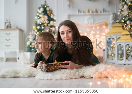 a young mother with a small son rested comfortably on sheep's clothing on the background of a fireplace and a Christmas tree