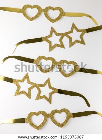 Cardboard golden eyeglasses in the shape of stars and hearts lying on a white table. Minimalistic style. Top view. Flat lay.