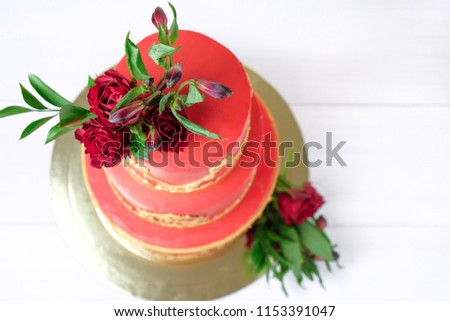 Three-tiered red wedding cream cake decorated with flowers and gold elements on a white wooden table. Picture for a menu or a confectionery catalog. Top view.