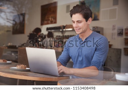 Young white man using his laptop at a table in a coffee shop