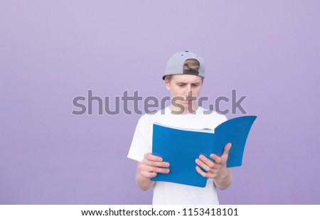 Young student in a white T-shirt read a book on a purple background. A student stands with a magazine on the background of a purple wall and reads. Learning the concept. isolated