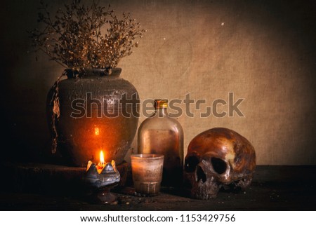 Human skull and candle with on wooden floor and old dirty wall background, and vase flower,and glass,and bottle of wine, still life concep
