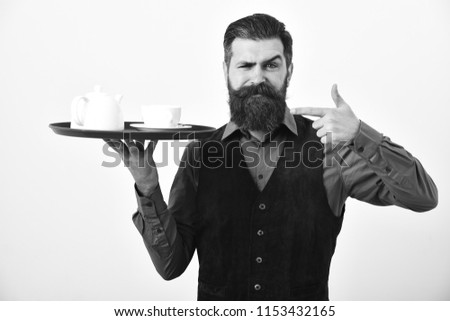 Man with beard and mustache holds tea on white background. Waiter points at tray with white tea cup and pot. Professional service concept. Barman with serious face serves coffee or tea.