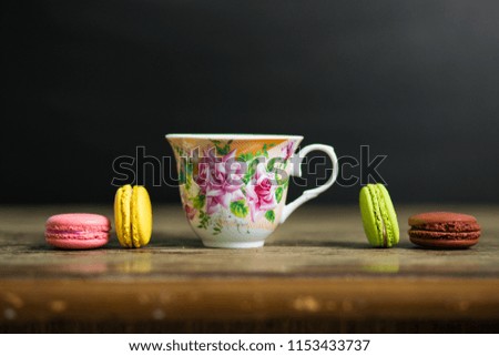Cup of coffee and french macaron on old wooden table with black background, good morning