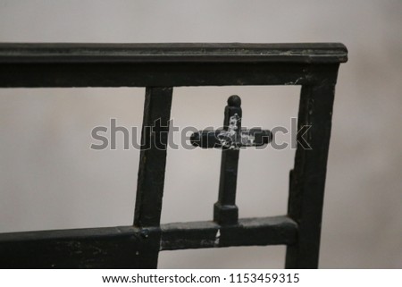 Close up view of a small metallic cross incorporated in a black forged gate. Religious sign located in a french church. Silhouette of a catholic symbol. Blur brown background. Abstract picture.