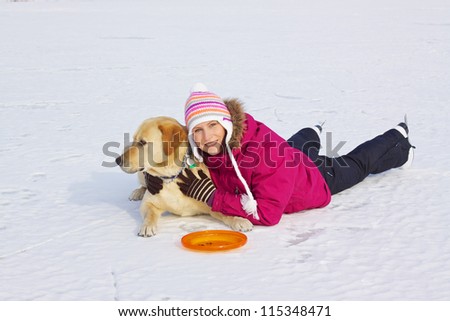 Beautiful young girl with ice skates laying with her dog in snow on frozen lake
