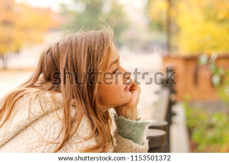 Portrait of beautiful pensive little girl daydreaming with chin on her hand in autumn park. Teenage dreams and hopes. Autumn melancholy.