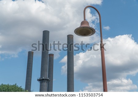 View looking at old factory smoke stacks with antique lamp post in foreground against pretty day time sky background party cloudy weather