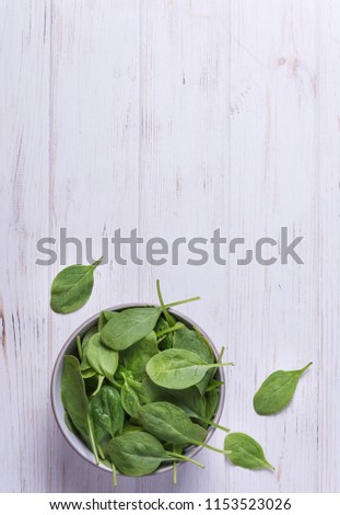 Fresh spinach in a bowl on white wooden background
