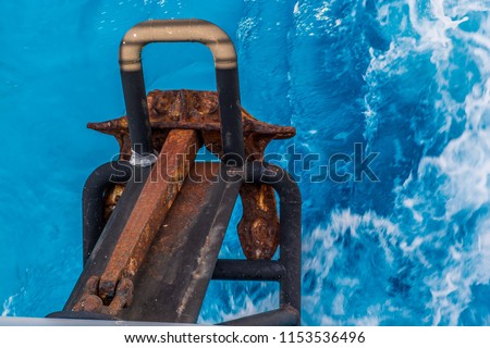 A small rusty anchor from above with beautiful blue water below