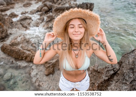 high angle view of beautiful happy girl in bikini top and straw hat standing with closed eyes on rocky beach in montenegro