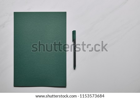 Green paper and pen on white marble background