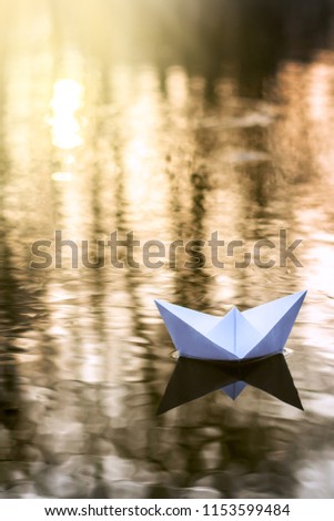 Alone paper boat sailing along the river at sunset. Concept of loneliness, abandonment, freedom
