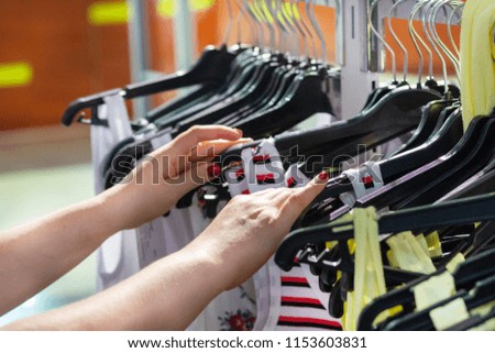 Female hands on touch a coat hanger with clothes in boutique. Shopping mall. Clothing store. The girl considers and chooses to herself clothes