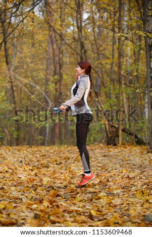 Full-length image of young woman jumping with rope at autumn forest