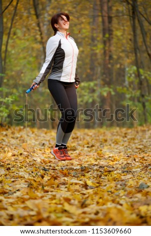 Photo of side view of sports woman jumping with rope at autumn forest