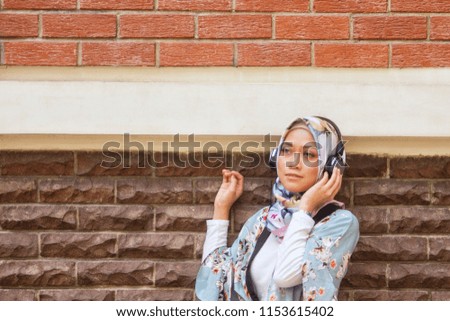 Young attractive Asian girl with hijab enjoying music from her wireless headphone 