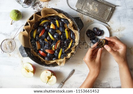 The process of making a fruit pie. Female hands hold the plum. Working conditions in the kitchen. Light photo