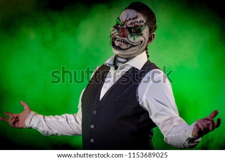 Portrait of a nicely dressed man wearing an evil clown mask with stitches and skull makeup underneath. Horror and Halloween themed, shot with theatrical lighting and effects