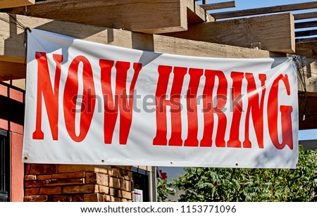 Large now hiring sign posted in the front of a business