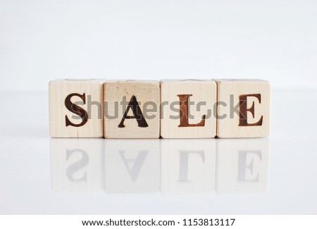 Word SALE made with wooden cubes, white background with reflection.