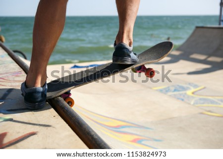 Skater boy rides on skateboard in skate park. Young skateboarder athlete practicing in mini ramp outdoor. Skateboarding contest in summer. Feet of rider skating in skatepark