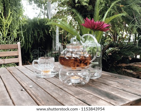 Exotic green tea with flowers in glass teapot and tea glass at garden burry bokeh background. (Selective focus)