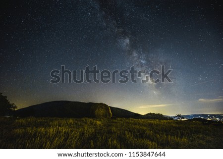 Beautiful view of starred night sky with milky way over a cultivated field with hay bale