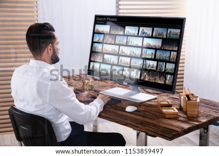 Young Male Photo Editor Searching Photos On Computer In Office