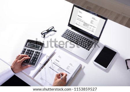 High Angle View Of Businessperson Calculating Invoice With Laptop On Desk Royalty-Free Stock Photo #1153859527